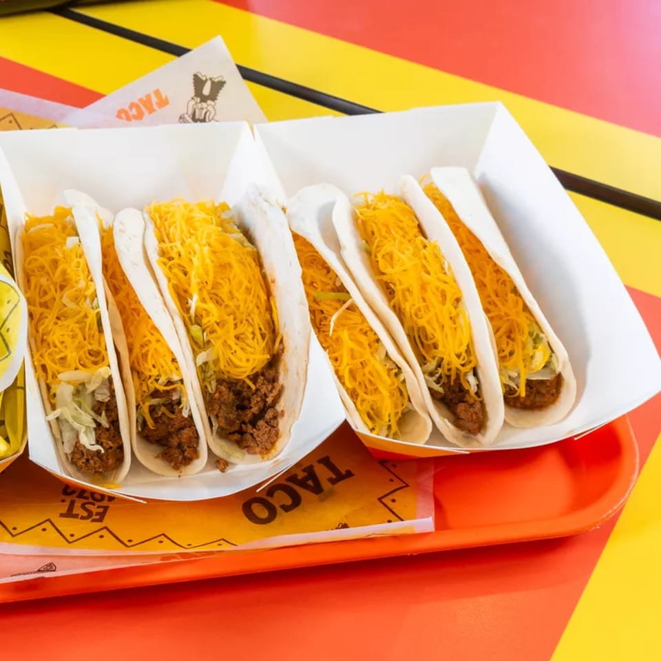 Two white paper trays filled with soft tacos, generously topped with shredded cheese and meat.