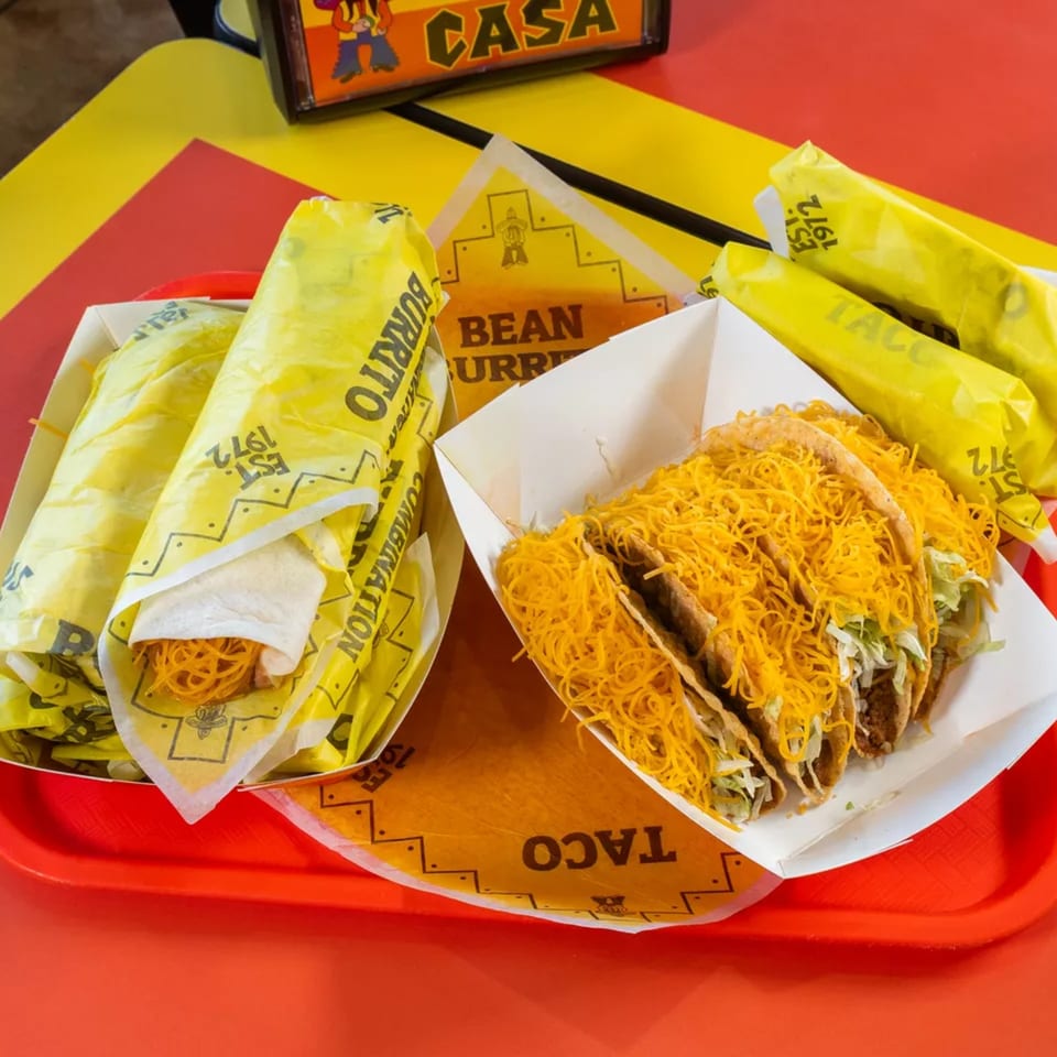 Tacos and burritos from Casa Garcia, with shredded cheese and lettuce, on a red tray.
