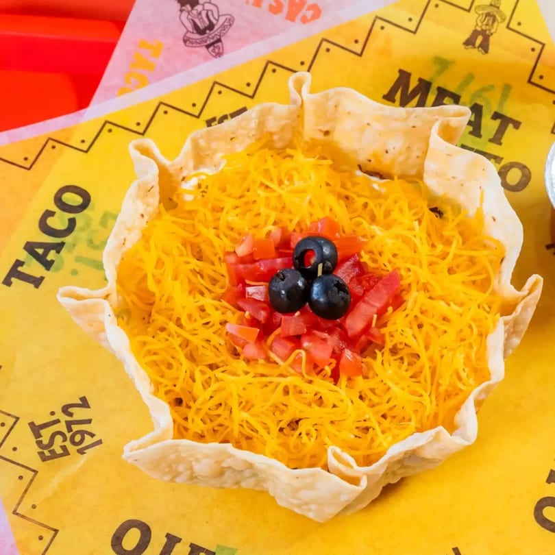Taco salad in a crispy tortilla bowl, topped with shredded cheese, diced tomatoes, and black olives.