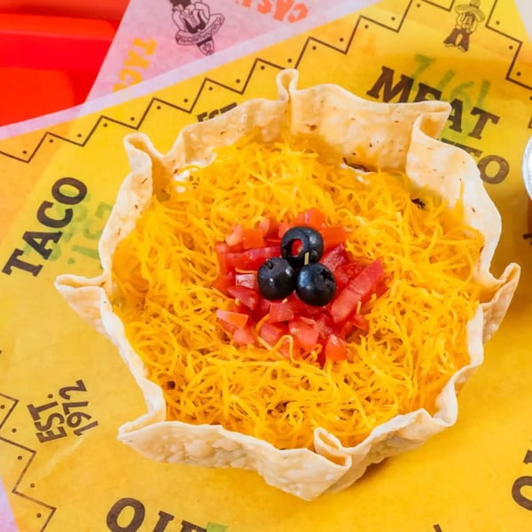 A taco salad in a crispy tortilla bowl, topped with shredded cheese, diced tomatoes, and black olives.