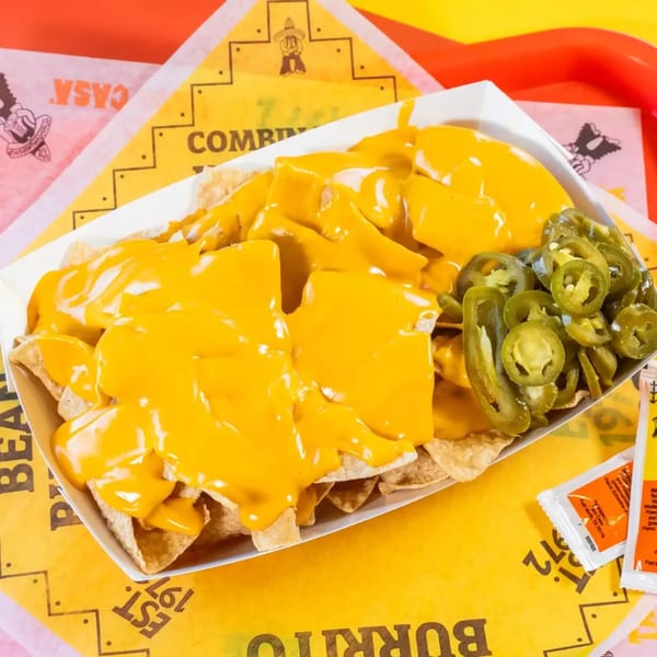 Nachos with melted cheese and sliced jalapeños in a white tray on a yellow and orange background.