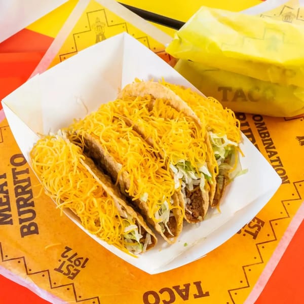 Four crispy tacos filled with meat, lettuce, and shredded cheese in a white tray.