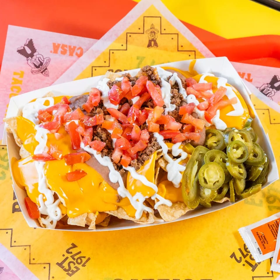 A tray of Taco Casa nachos with cheese, ground beef, tomatoes, sour cream, and jalapeños.