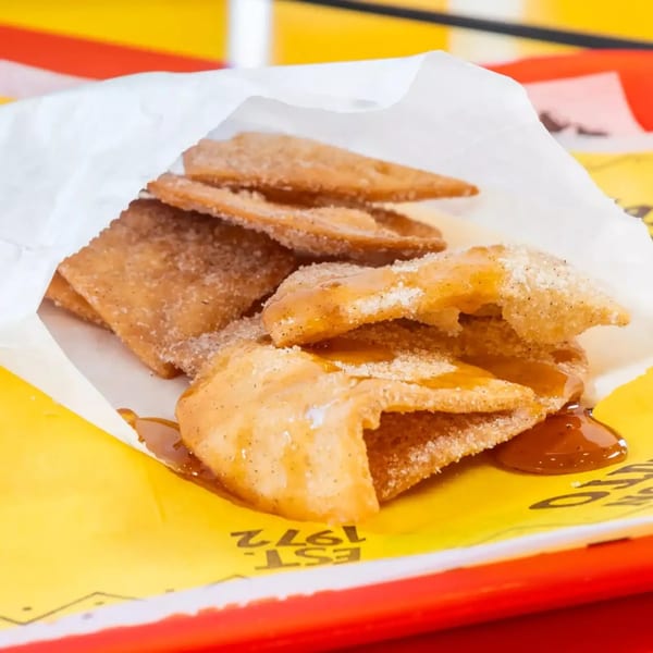 Crispy cinnamon sugar chips drizzled with caramel sauce, served in a white paper bag on a yellow tray.