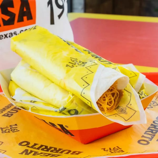 Three yellow-wrapped burritos, one open to show noodles, in a branded paper tray on a red and yellow surface.