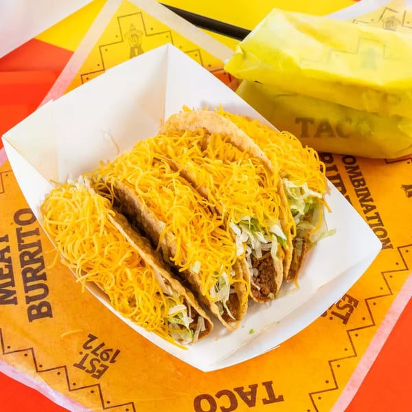 Four crispy tacos filled with meat, lettuce, and shredded cheese in a white tray.