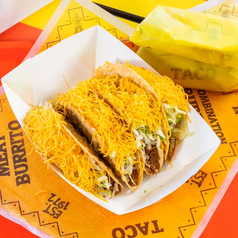 Four crispy tacos filled with meat, lettuce, and shredded cheese in a white tray.