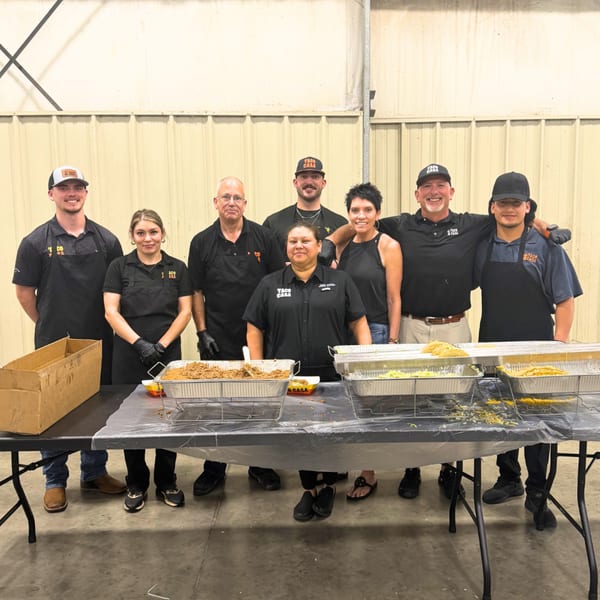 Eight Taco Casa employees stand behind a table laden with catering trays of food.