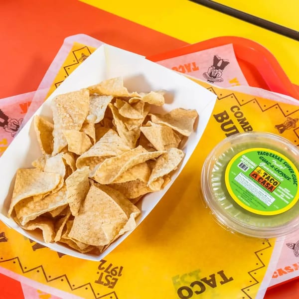 Taco Casa tortilla chips in a white tray next to a container of guacamole on a branded paper liner.