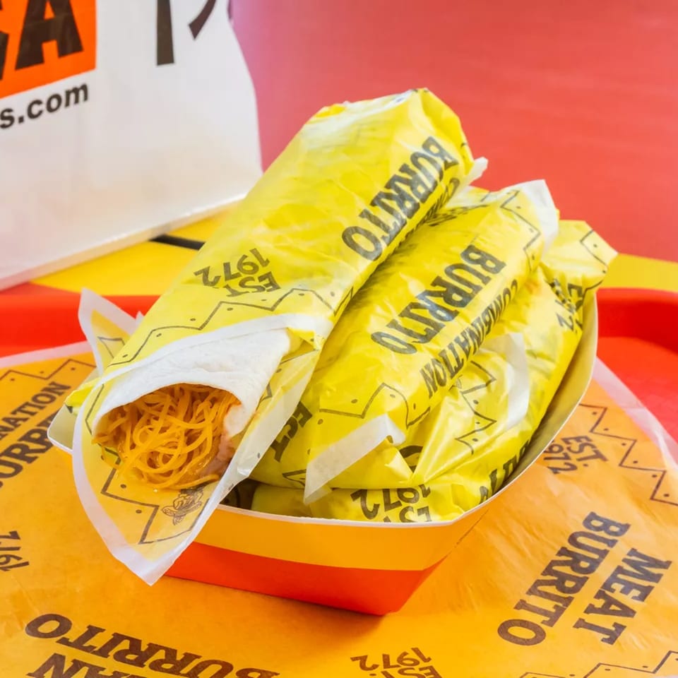 Several yellow-wrapped burritos in a red and yellow tray, one partially unwrapped showing noodles.
